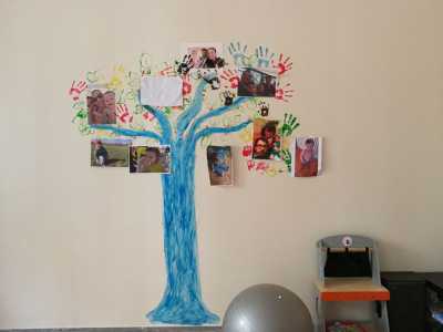 Su una parete si trova la raffigurazione di un albero colorato di blu con le foto appese dei genitori